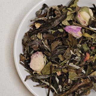 Liście białej herbaty z pączkami i płatkami róży na talerzyku.