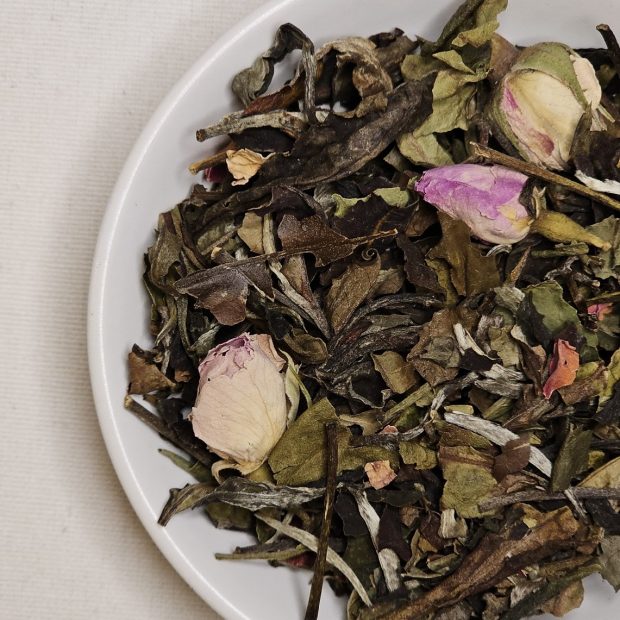 Liście białej herbaty z pączkami i płatkami róży na talerzyku.
