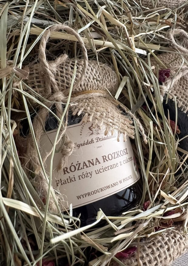 Zbliżenie na słoik płatków róż w cukrze w zestawie prezentowym, otoczony naturalnym siankiem i jutą.