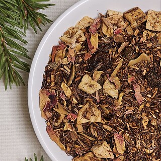 Rooibos Zimowy Czar z jabłkiem, rodzynkami, cynamonem i migdałami na białym talerzyku, w zimowej aranżacji.