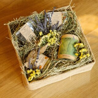 Zestaw prezentowy z lawendową herbatą, suszem owocowym, ziołami i miodem pomarańczowym w pudełku ozdobionym jutą, siankiem i kwiatami.