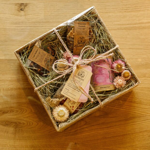 Zestaw prezentowy w pudełku z herbatami, ziołami w puszce, miodem, ozdobiony naturalnymi dodatkami - kwiatami i siankiem.