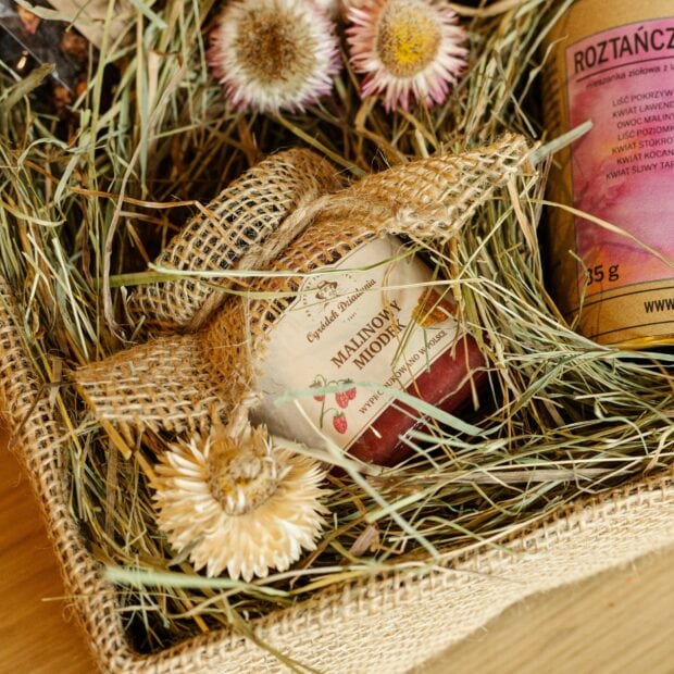Miodek malinowy otoczony naturalnymi dekoracjami w postaci sianka i kwiatów.
