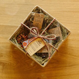 Pudełko zawiązane sznurkiem ozdobnym, w środku bertay w transparentnych torebkach otoczone siankiem i kwiatami