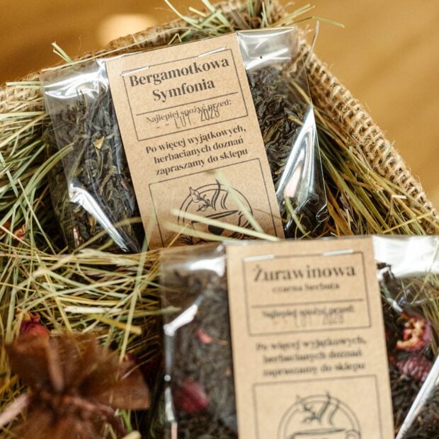 Dwa opakowania transparetne z herbatą w otoczeniu sianka, w pudełku ozdobnym.