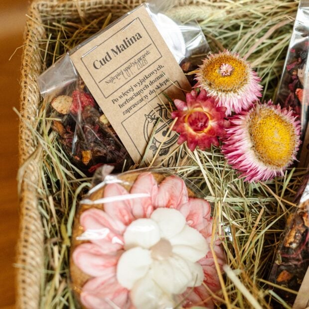 Susz owocowy w transparentnej torebce w towarzystwie pierniczka ręcznie zdobionego, w otoczeniu sianka i kwiatów